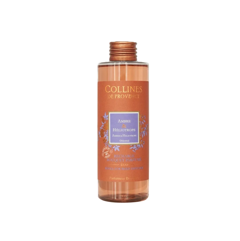 Recharge 200ml pour diffuseur Colline de Provence Ambre HĂ©liotrope, flacon Ă©purĂ© posĂ© Ă cĂŽtĂ© de tiges en bois et dâun diffuseur vide.